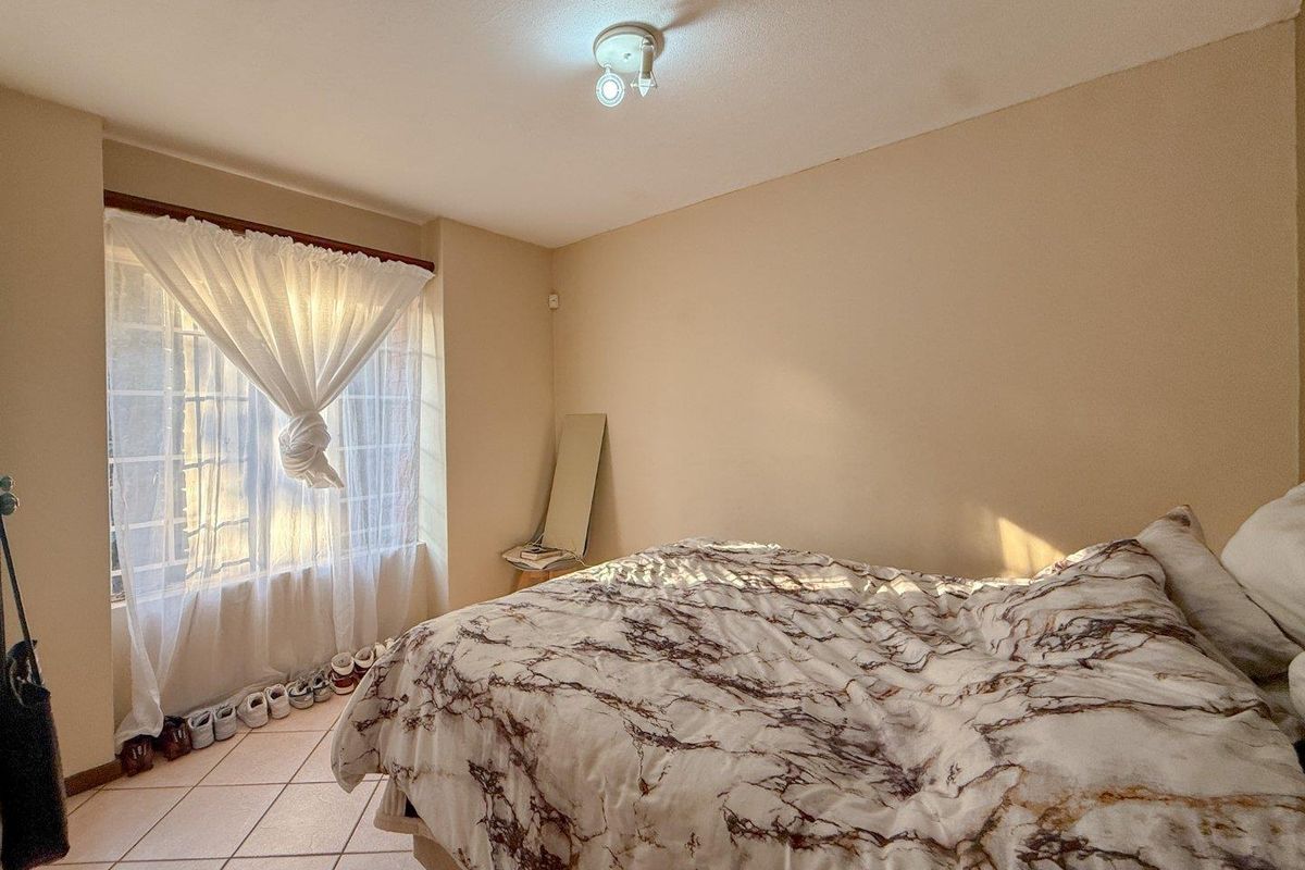 A bedroom featuring tiled flooring, a window with security bars, and a central ceiling light fixture.