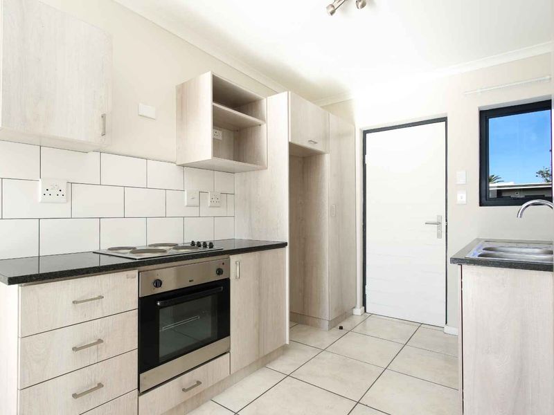 Modern kitchen featuring light wood-grain cabinetry, granite countertops, subway tile backsplash, and built-in oven with electric hob.