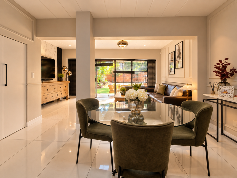 A bright and modern open-plan living and dining area featuring polished tile floors, elegant wall moulding, and large sliding doors leading to the garden.