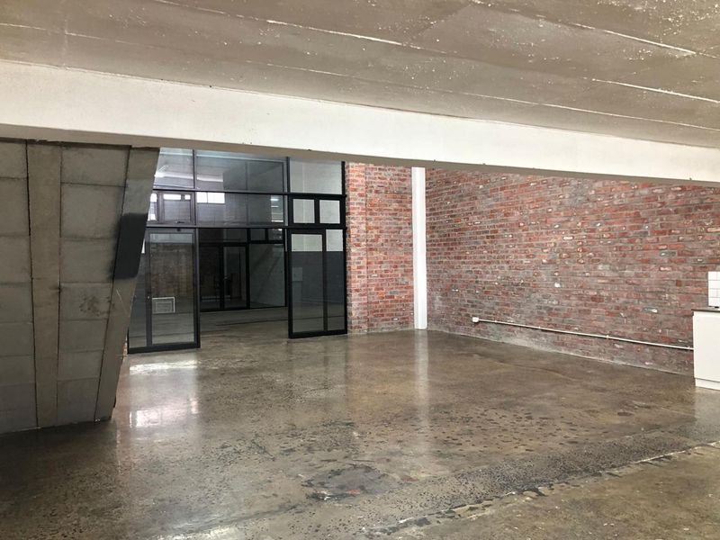 Spacious open-plan industrial-style area featuring exposed brick walls, polished concrete floors, and a concrete staircase with modern steel-framed glass partitions.