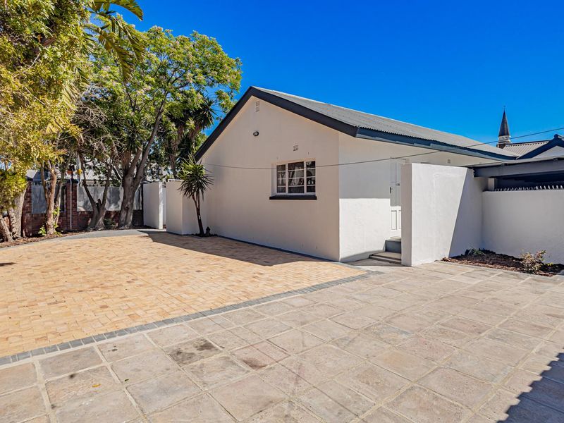 A well-maintained rear exterior view featuring a paved driveway, boundary walls, and a clean building facade under a clear blue sky.