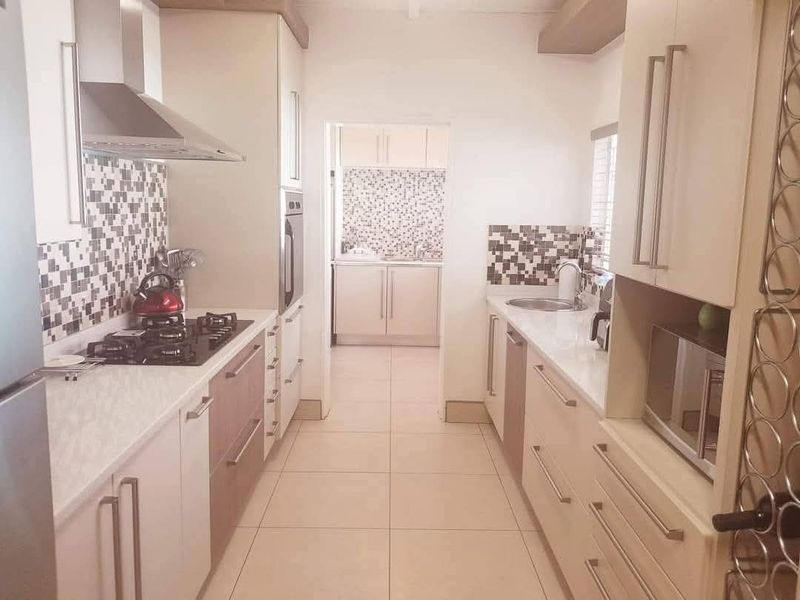 Modern galley-style kitchen featuring stone countertops, gas hob, built-in oven, and a separate scullery area with matching cabinetry and mosaic tile finishes.