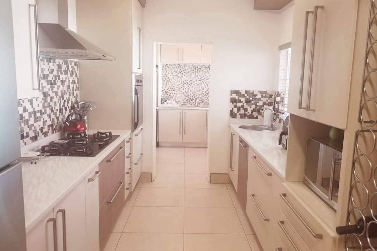 Modern galley-style kitchen featuring stone countertops, gas hob, built-in oven, and a separate scullery area with matching cabinetry and mosaic tile finishes.