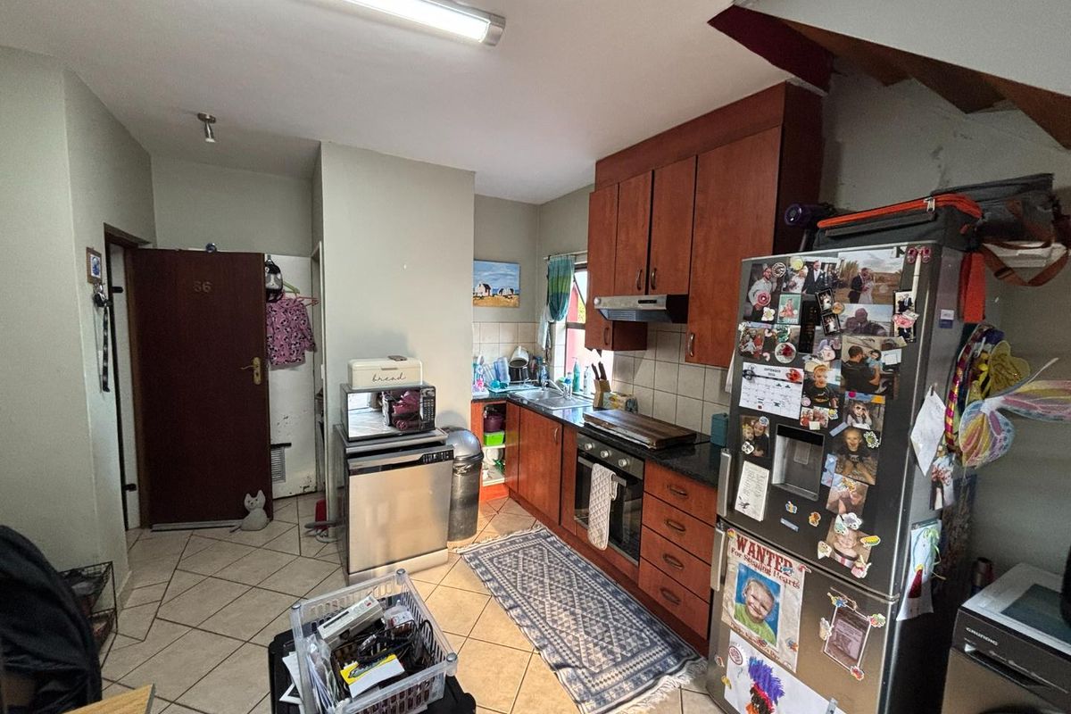 A functional kitchen featuring wooden cabinetry, built-in oven and hob, tiled backsplash, and tiled flooring, offering a practical layout for daily meal preparation.