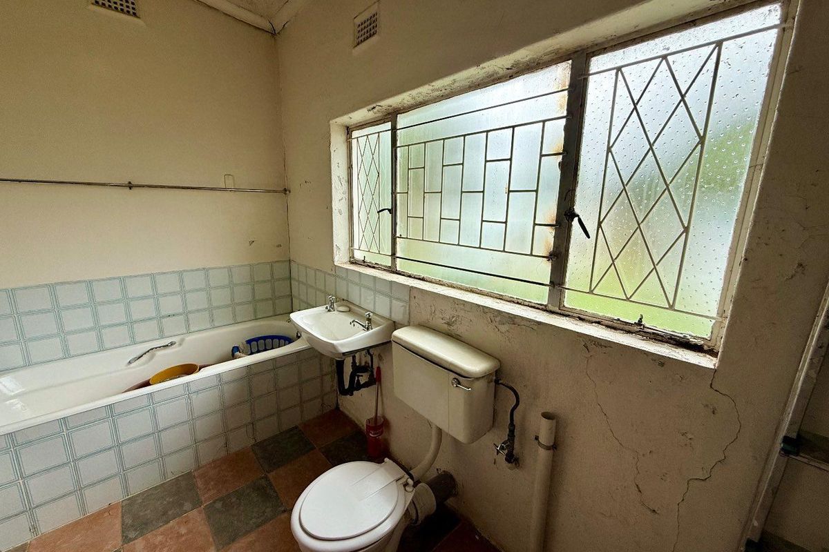 A dated bathroom featuring a standard bathtub, wall-mounted basin, and toilet, requiring significant renovation and cosmetic updates to restore functionality and aesthetic appeal.
