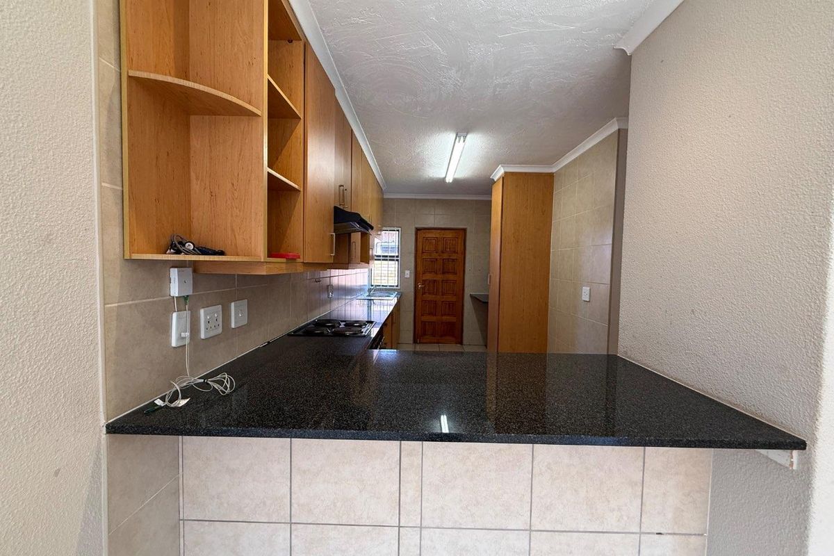 A functional kitchen featuring dark granite countertops, light wood cabinetry, a built-in hob, and a breakfast bar overlooking the living area.