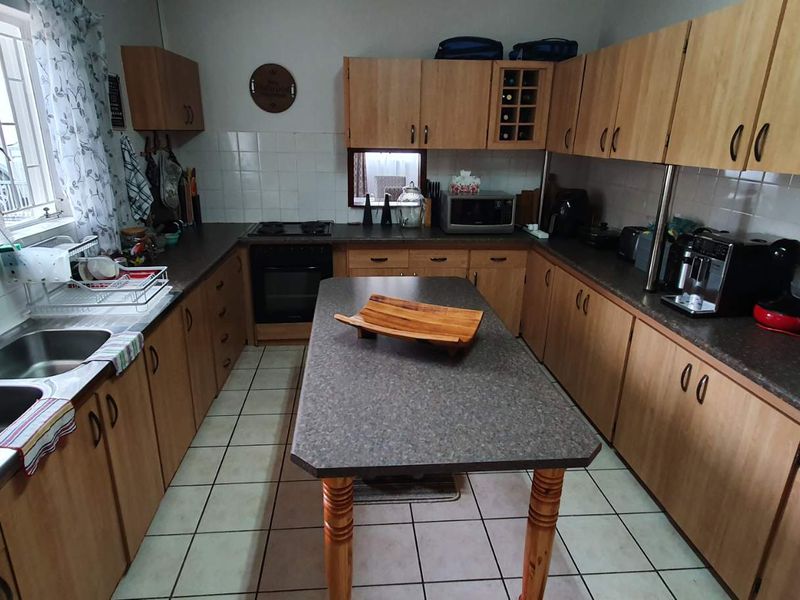 Functional kitchen featuring laminate cabinetry, a central island, double stainless steel sink, built-in oven, and tiled flooring with a tiled backsplash.