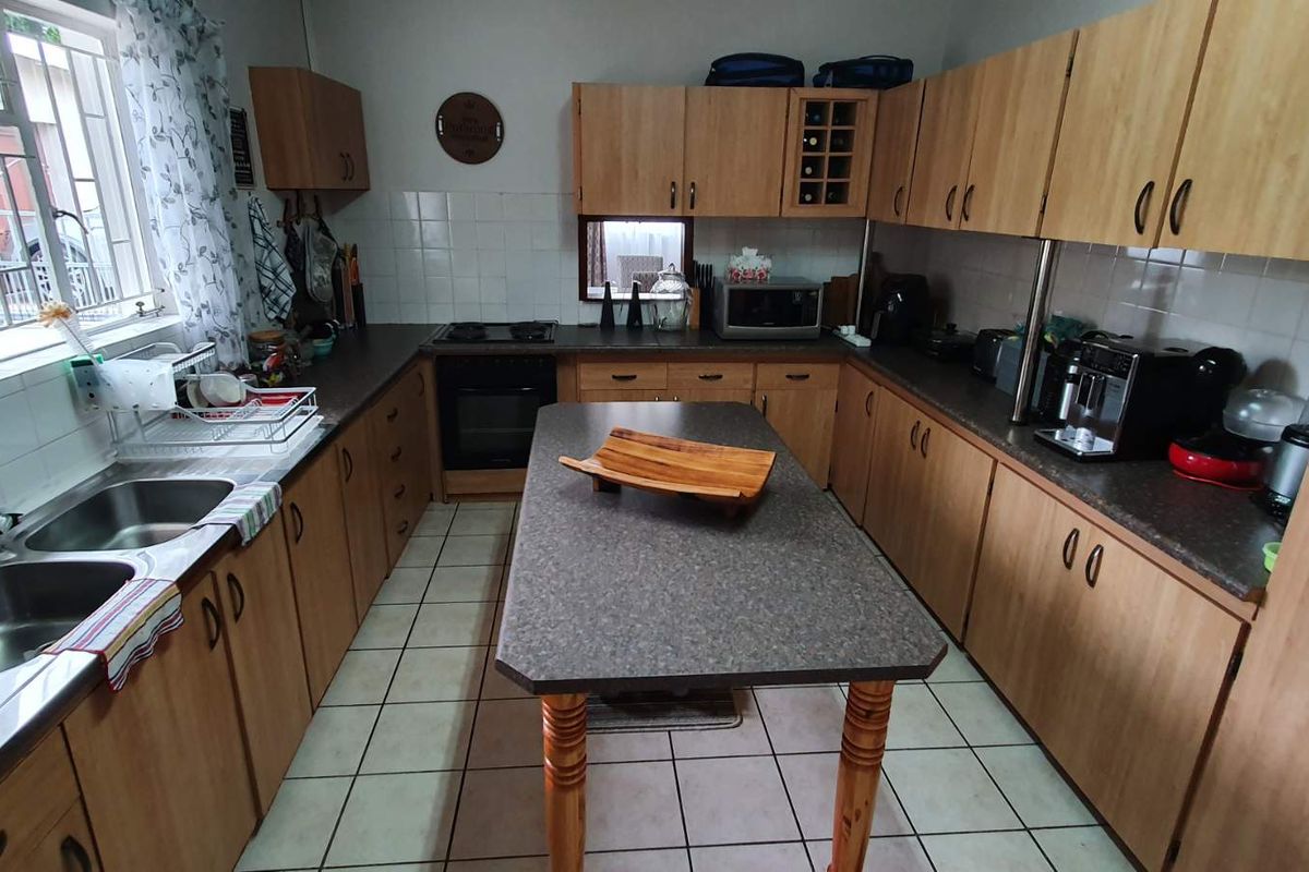Functional kitchen featuring laminate cabinetry, a central island, double stainless steel sink, built-in oven, and tiled flooring with a tiled backsplash.