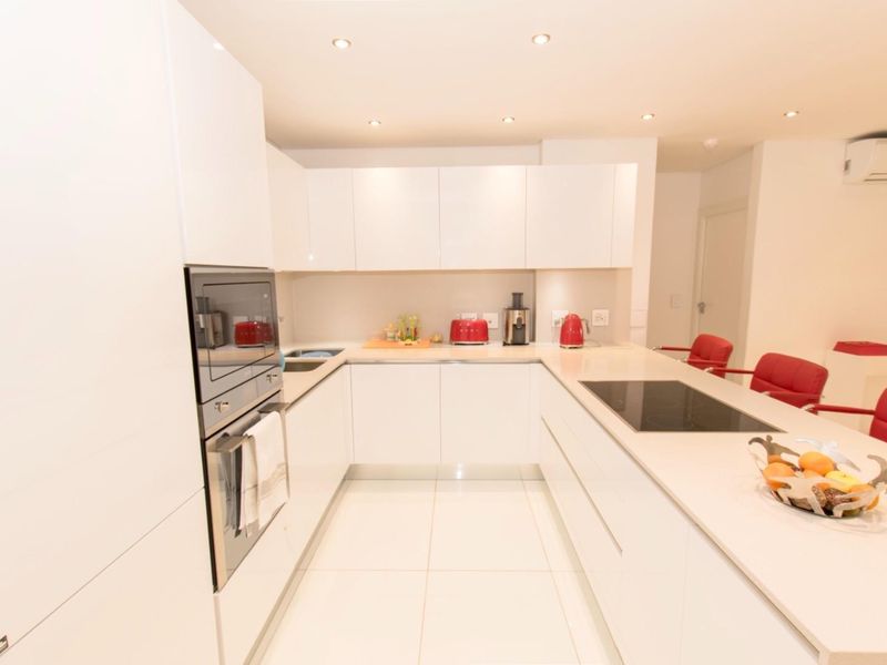 Modern white kitchen featuring sleek handleless cabinetry, integrated appliances, induction cooktop, and recessed lighting in an open-plan layout.