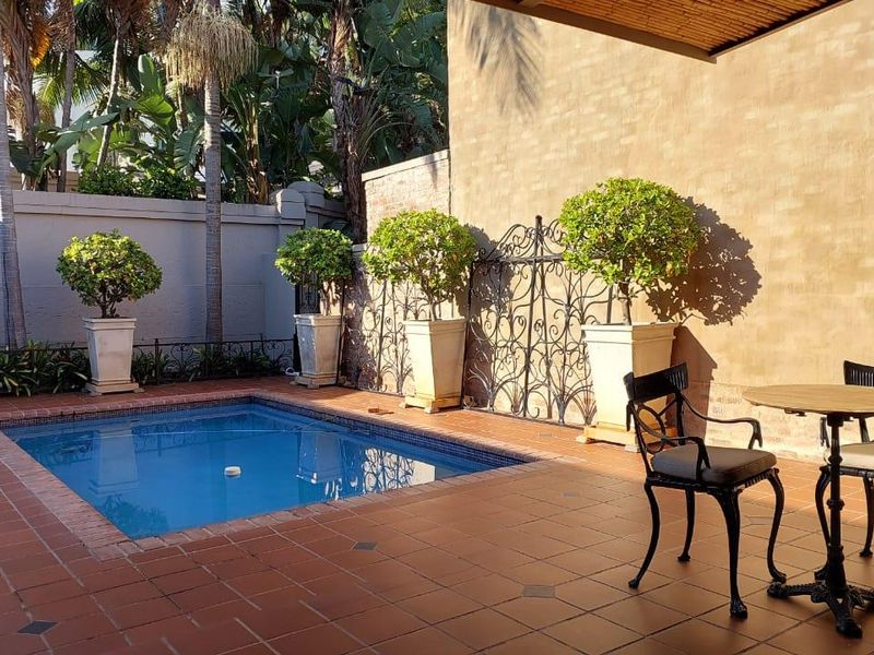 A private outdoor pool area featuring a tiled patio, perimeter boundary wall, and decorative wrought iron gate, perfect for relaxation and outdoor entertaining.