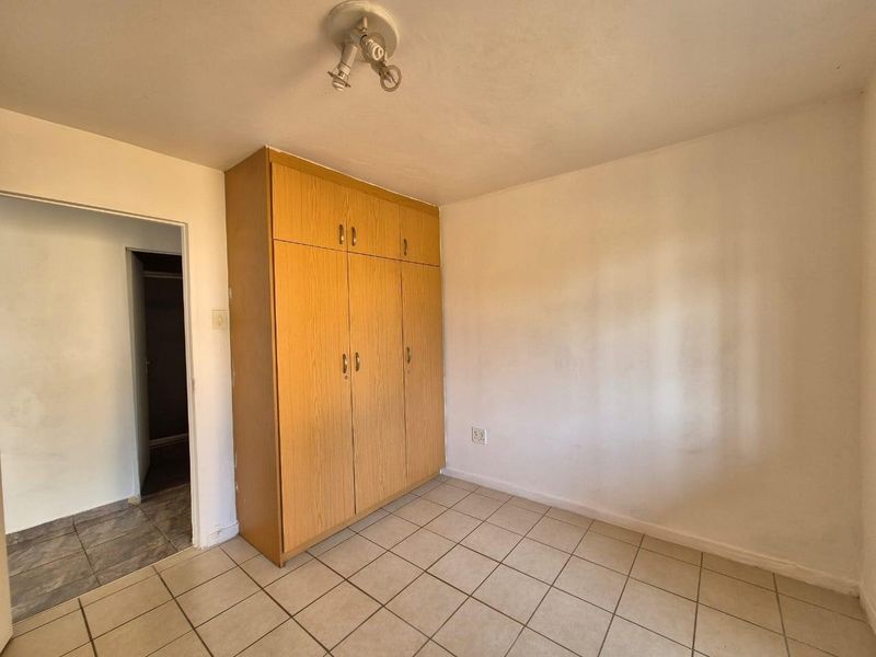 A vacant bedroom featuring built-in wooden cupboards and tiled flooring, offering a blank canvas for personalization.