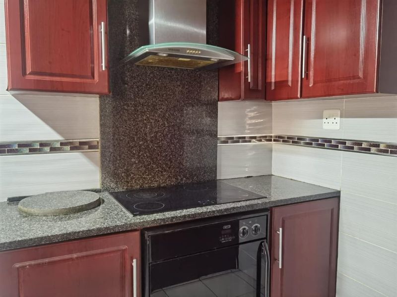 A functional kitchen featuring dark wood cabinetry, granite countertops, a built-in oven, electric hob, and a modern stainless steel extractor fan.
