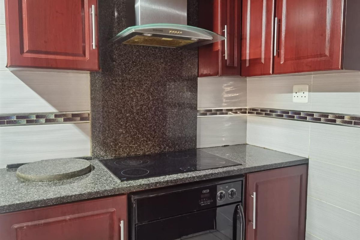 A functional kitchen featuring dark wood cabinetry, granite countertops, a built-in oven, electric hob, and a modern stainless steel extractor fan.