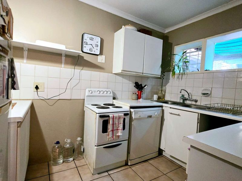 A functional kitchen featuring white cabinetry, tiled splashbacks, a stainless steel sink, and tiled flooring, offering a practical layout for daily meal preparation.