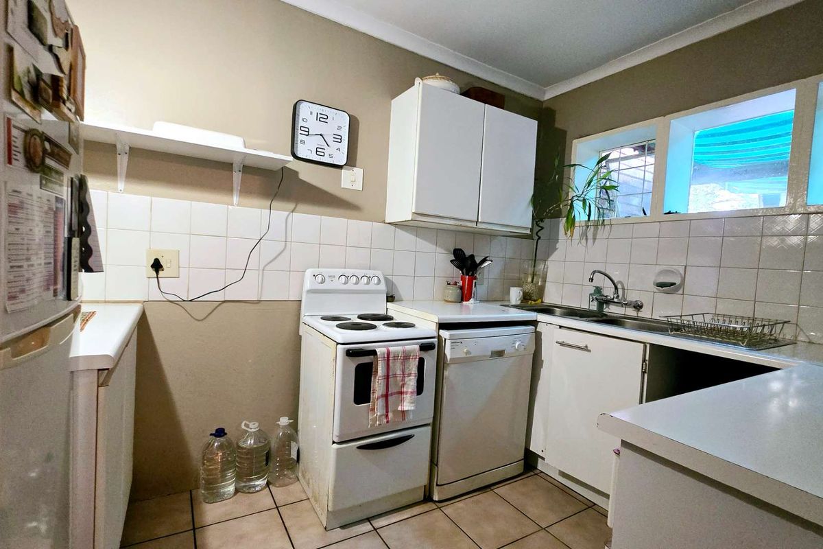A functional kitchen featuring white cabinetry, tiled splashbacks, a stainless steel sink, and tiled flooring, offering a practical layout for daily meal preparation.