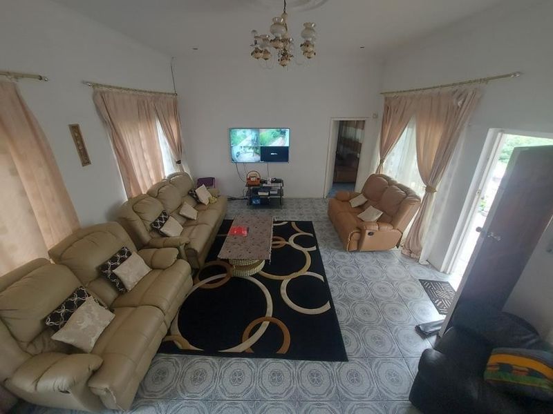 A spacious living room featuring ceramic floor tiles, a decorative ceiling rose with a chandelier, and dual access points to the exterior.