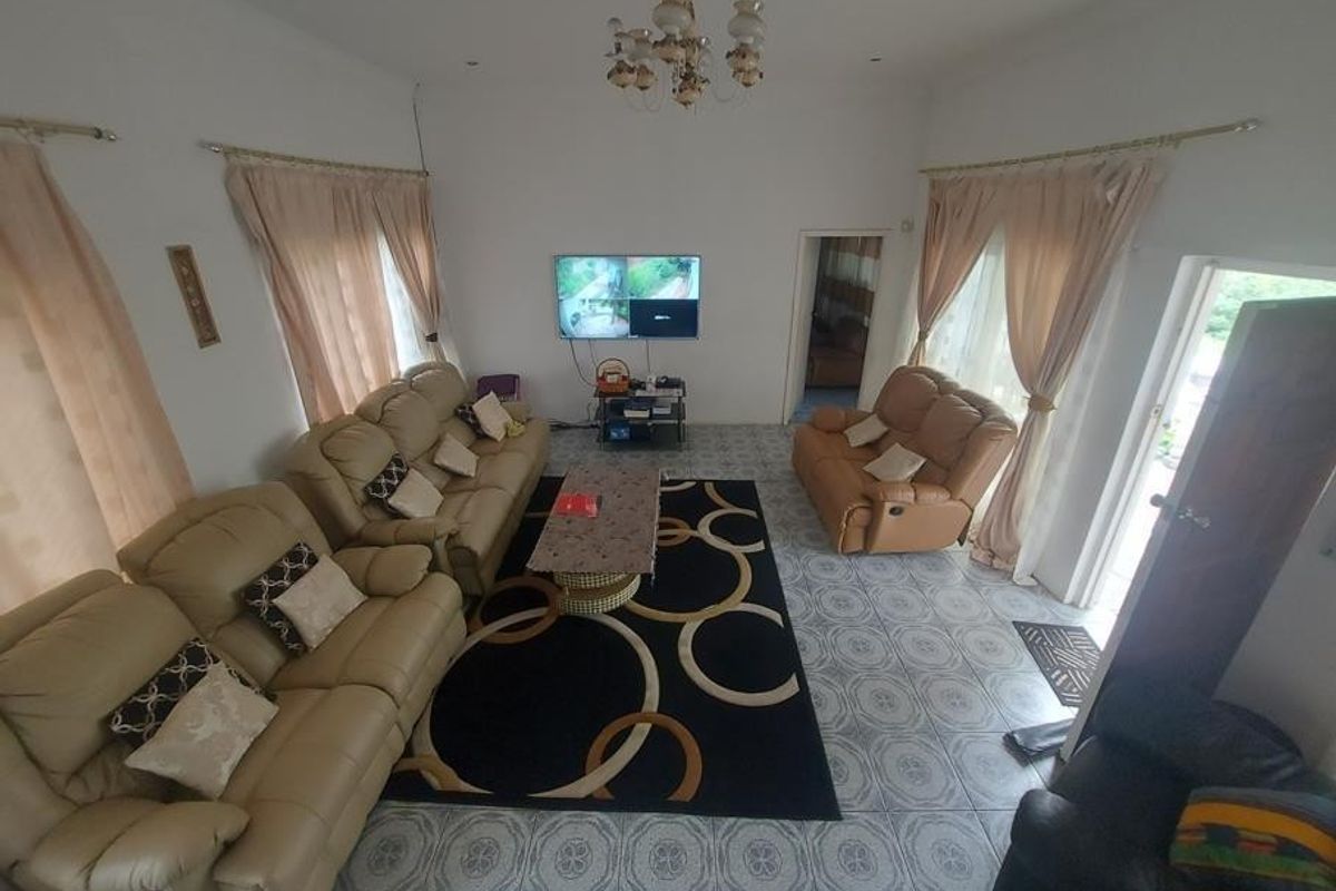A spacious living room featuring ceramic floor tiles, a decorative ceiling rose with a chandelier, and dual access points to the exterior.