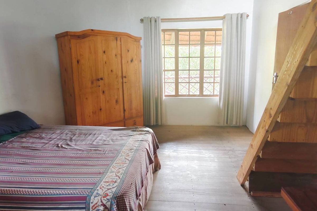 A bedroom featuring timber flooring, a wooden staircase leading to an upper level, and a window with natural light.