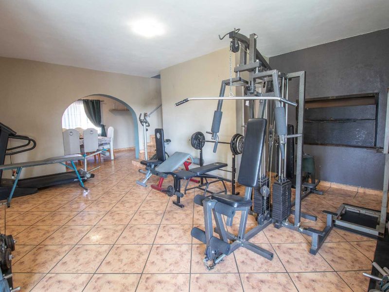 A multi-purpose room currently utilized as a home gym, featuring ceramic tile flooring and an arched entryway leading to an adjacent space.