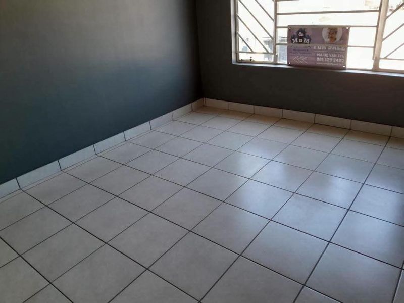 An empty living area featuring neutral tiled flooring and a window fitted with security bars.
