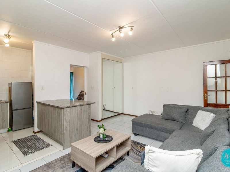 Open plan living area featuring a compact kitchen with granite countertops and a built-in mirrored wardrobe, finished with neutral tiled flooring throughout.