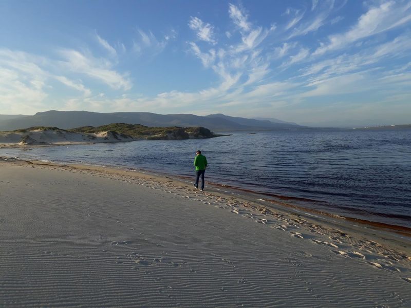 A scenic view of the coastline featuring sandy dunes, calm water, and distant mountains, highlighting the natural landscape of the vacant land property.