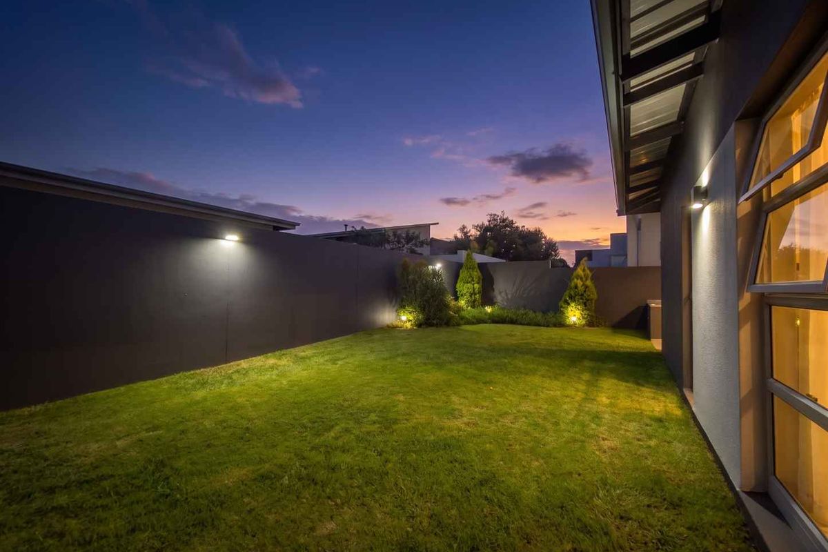 A well-maintained rear garden featuring a manicured lawn, perimeter boundary walls, and integrated outdoor lighting, captured during twilight.