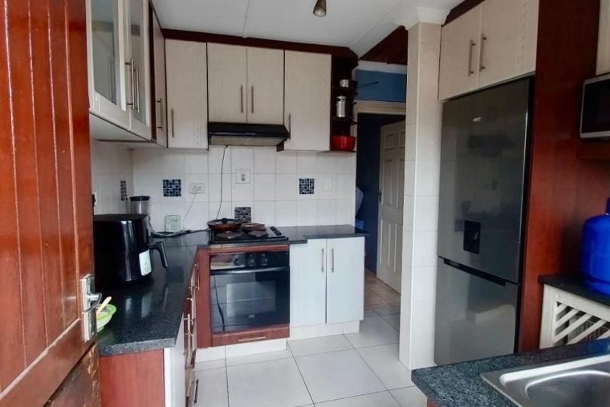 A functional kitchen featuring built-in cabinetry, granite countertops, a built-in oven with hob, extractor fan, and tiled flooring.