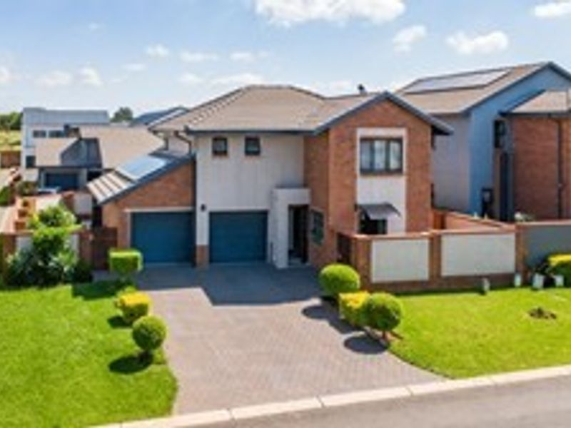 Aerial view of a modern double-story residential home featuring a paved driveway, double garage, and well-maintained garden with boundary walling.