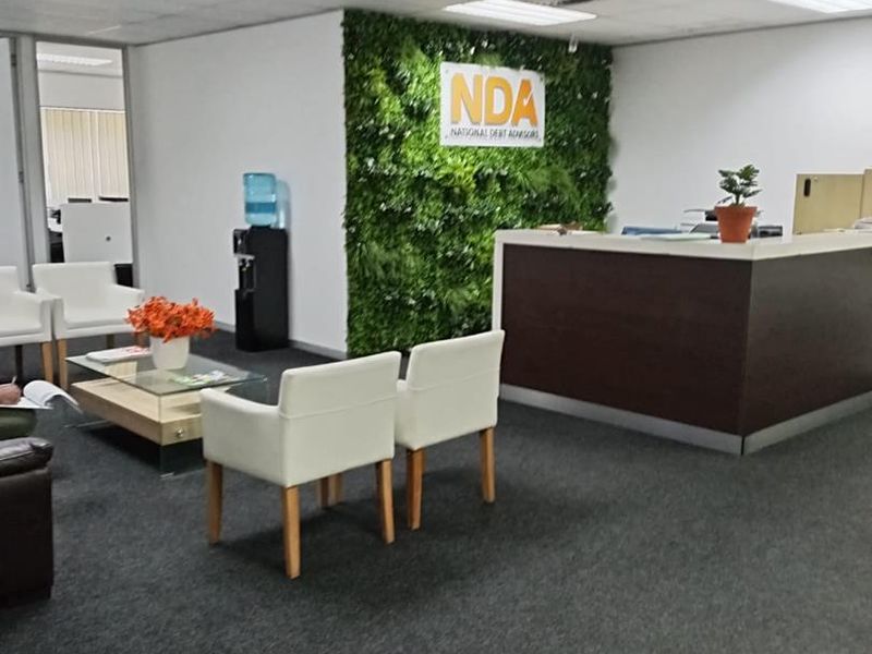 A professional office reception area featuring a built-in desk, carpeted flooring, suspended ceiling, and a decorative green wall feature.