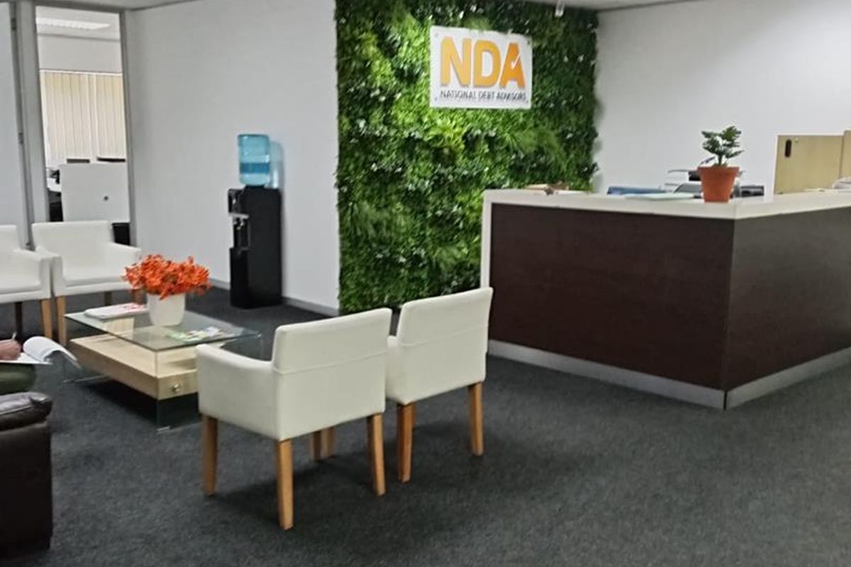 A professional office reception area featuring a built-in desk, carpeted flooring, suspended ceiling, and a decorative green wall feature.