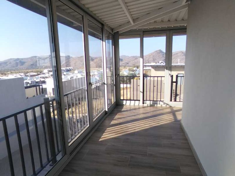 A modern, covered balcony featuring tiled flooring, large sliding glass doors, and a metal balustrade, offering expansive views of the surrounding landscape.