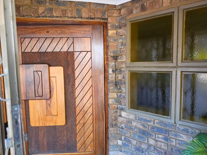 A detailed view of a solid wood front door with decorative paneling, set within a textured brick facade and featuring obscured glass windows.