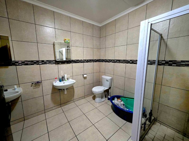 A functional bathroom featuring tiled walls with a decorative border, a shower enclosure, a toilet, and a wall-mounted basin.
