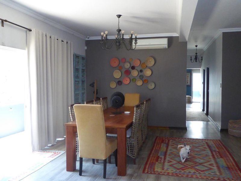 A well-maintained dining area featuring laminate flooring, cove molding, a decorative chandelier, and a wall-mounted split-system air conditioner.