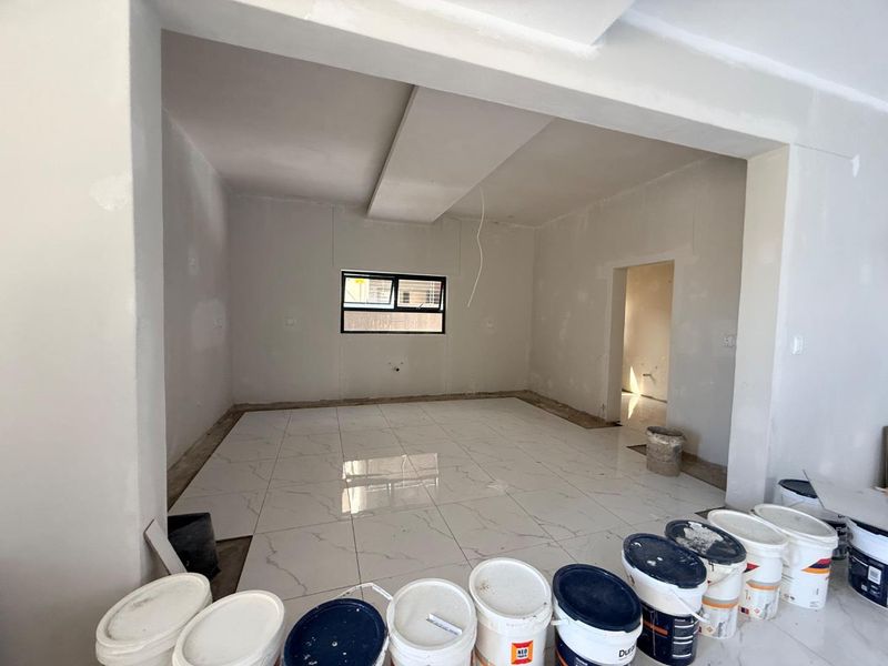 An open-plan living area currently under renovation, featuring newly laid porcelain floor tiles, unfinished wall surfaces, and a modern dropped ceiling bulkhead.