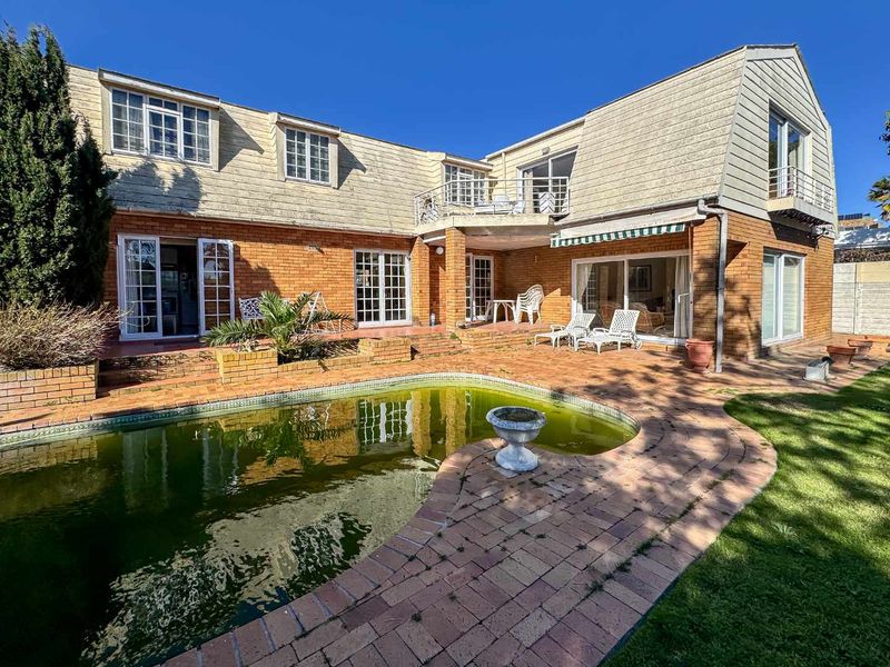 Rear exterior view of a two-story brick house featuring a swimming pool, paved patio area, upper-level balcony, and multiple access points via glass doors.