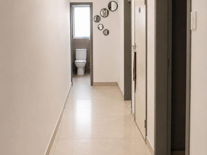 A clean, well-lit hallway featuring neutral tiled flooring and access to adjacent rooms, including a view into a bathroom.