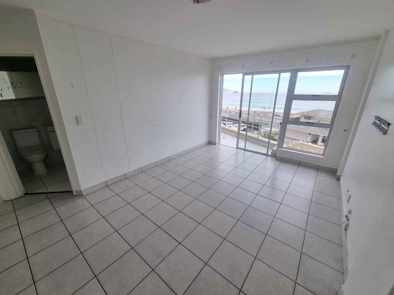 An empty living area featuring tiled flooring and large sliding glass doors that provide natural light and access to a balcony with ocean views.