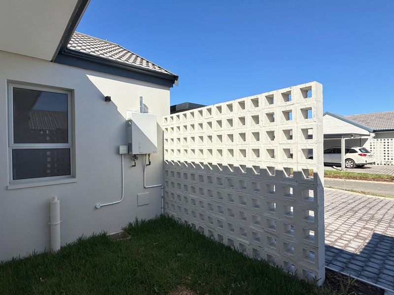 Rear exterior view featuring a decorative breeze block privacy screen, gas geyser installation, and paved driveway access.