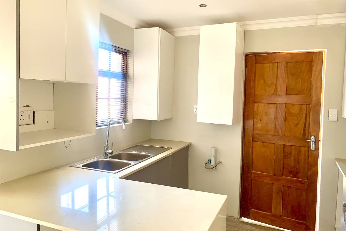 A clean, modern kitchen featuring white cabinetry, quartz countertops, a double bowl sink, and a classic timber door, offering a bright and functional workspace.