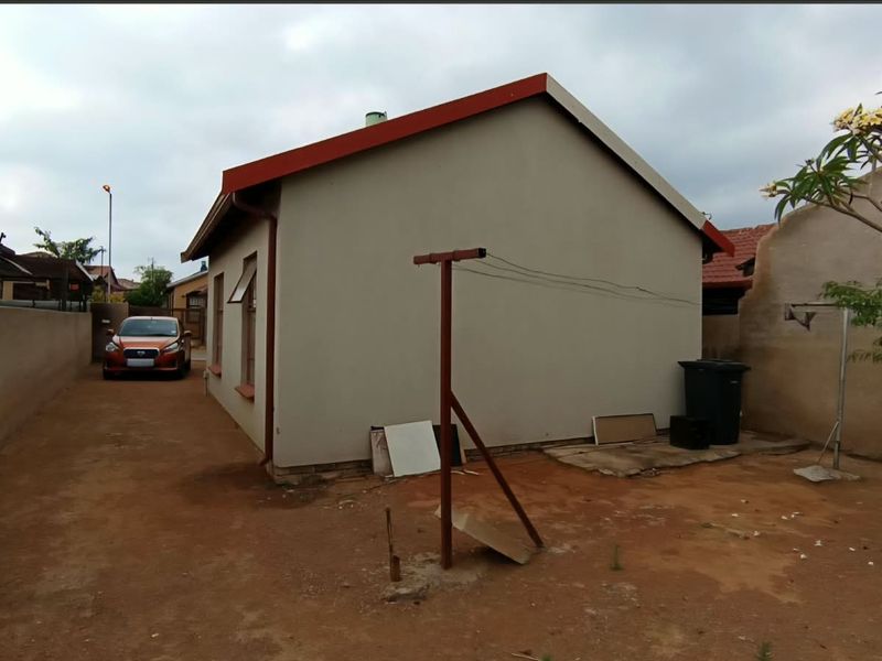 Rear view of the property showing the exterior wall, metal roof, and unpaved yard area.