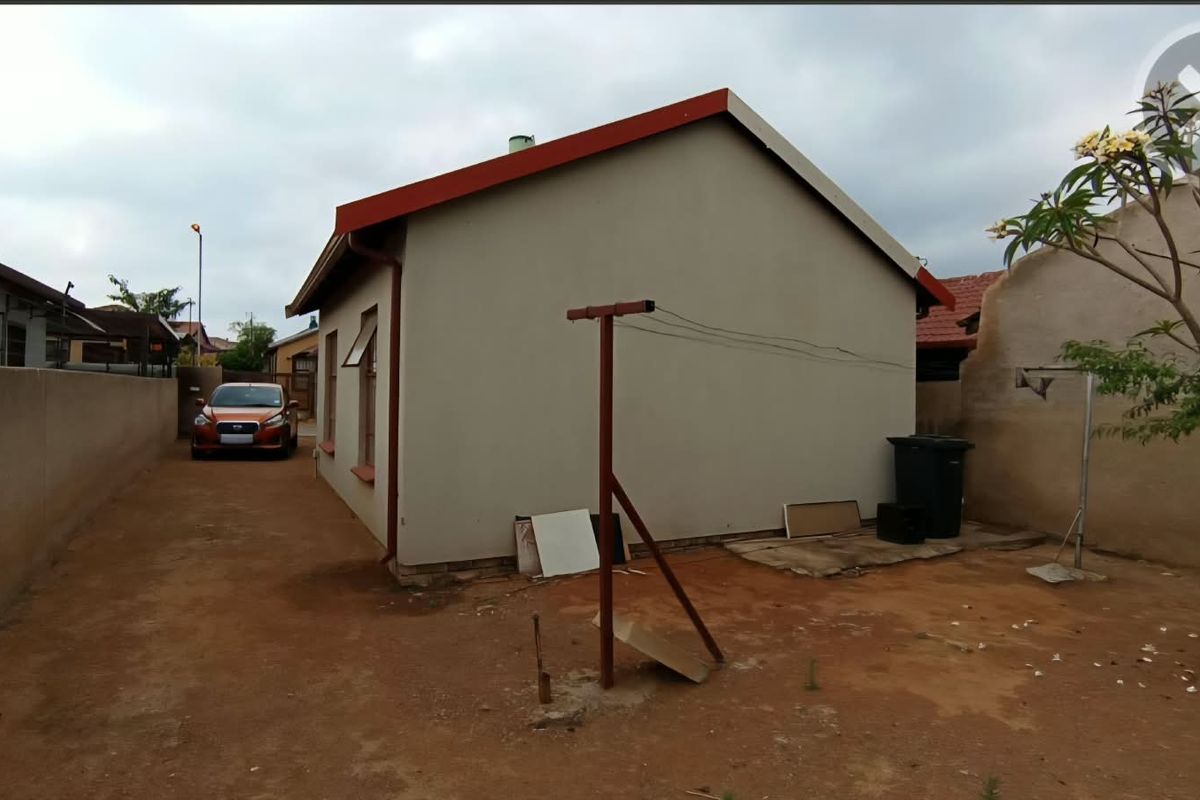 Rear view of the property showing the exterior wall, metal roof, and unpaved yard area.