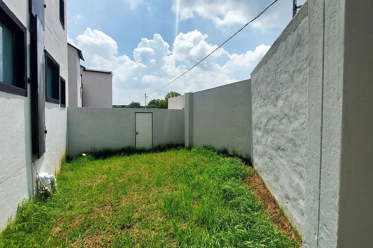 A private rear garden area featuring a lawn, enclosed by high perimeter walls with a small access door.