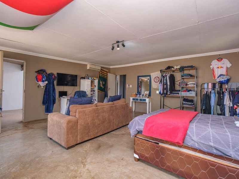A spacious bedroom featuring a concrete floor, coved ceiling, and wall-mounted air conditioning unit, offering potential for modernization and improved finishes.