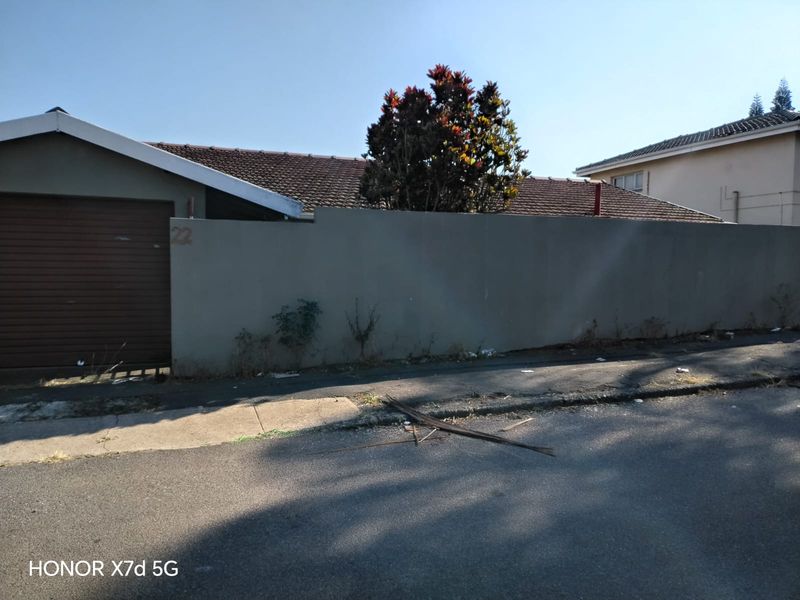 Front exterior view of the property featuring a garage door and a boundary wall with visible signs of wear and maintenance needs.
