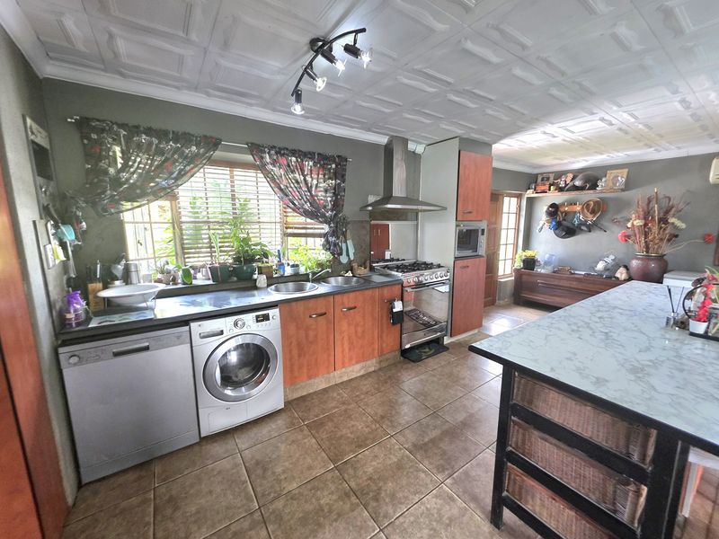 A functional kitchen featuring wooden cabinetry, a gas stove with extractor fan, double sink, and tiled flooring, offering ample workspace and integrated appliance storage.
