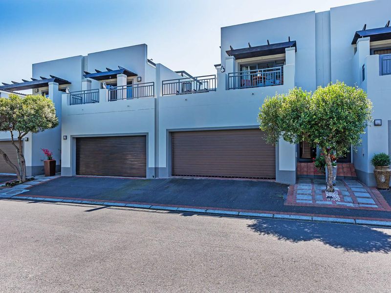 Modern townhouse facade featuring double garages, upper-level balconies with metal railings, and paved driveway access.