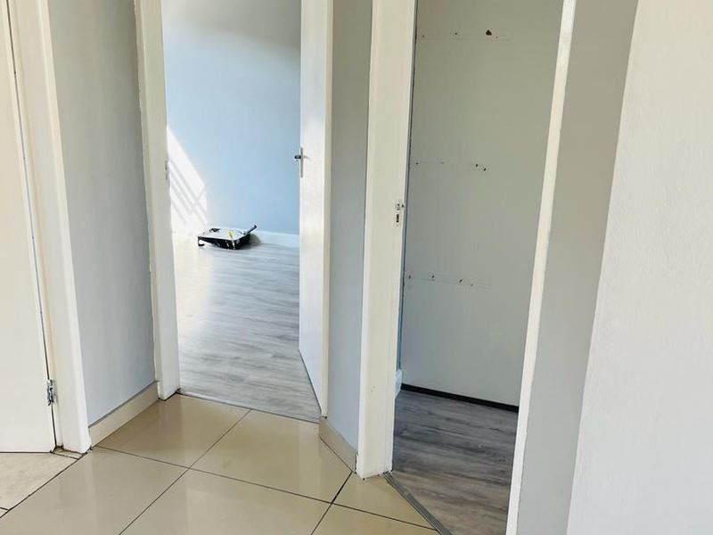 A bright, empty hallway featuring neutral tiled flooring and access to adjacent rooms with laminate flooring.