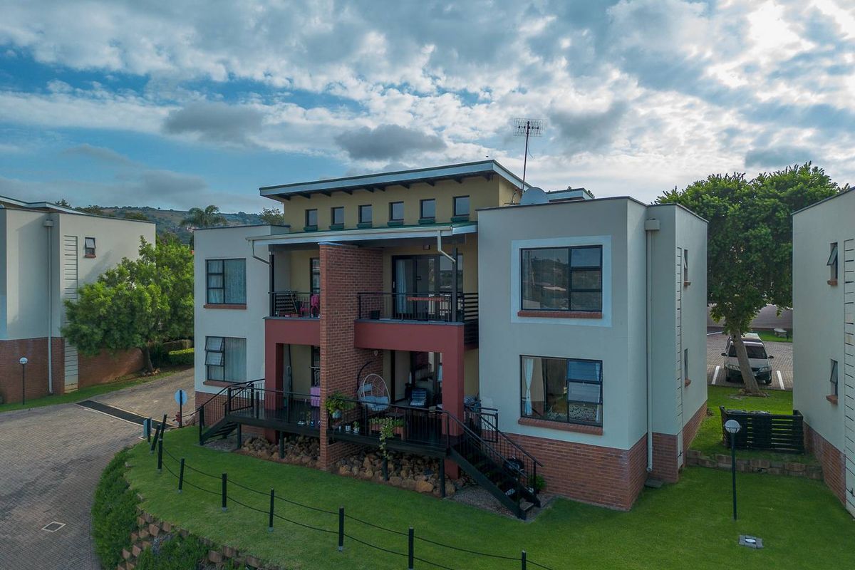 An aerial view of a multi-story apartment building featuring brick and plaster facade, private balconies with metal railings, and landscaped garden surroundings.